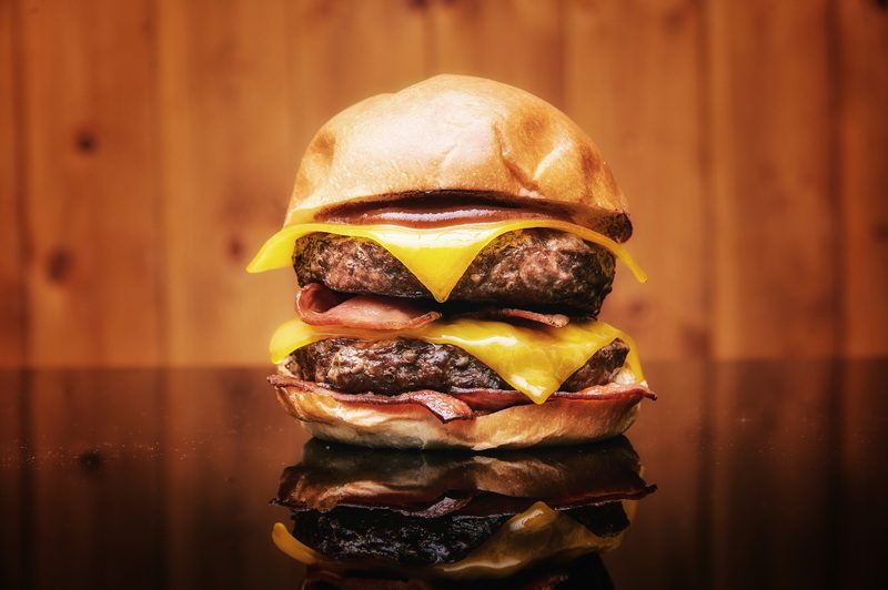 Hamburguesa doble con queso fundido y bacon reflejada sobre superficie oscura