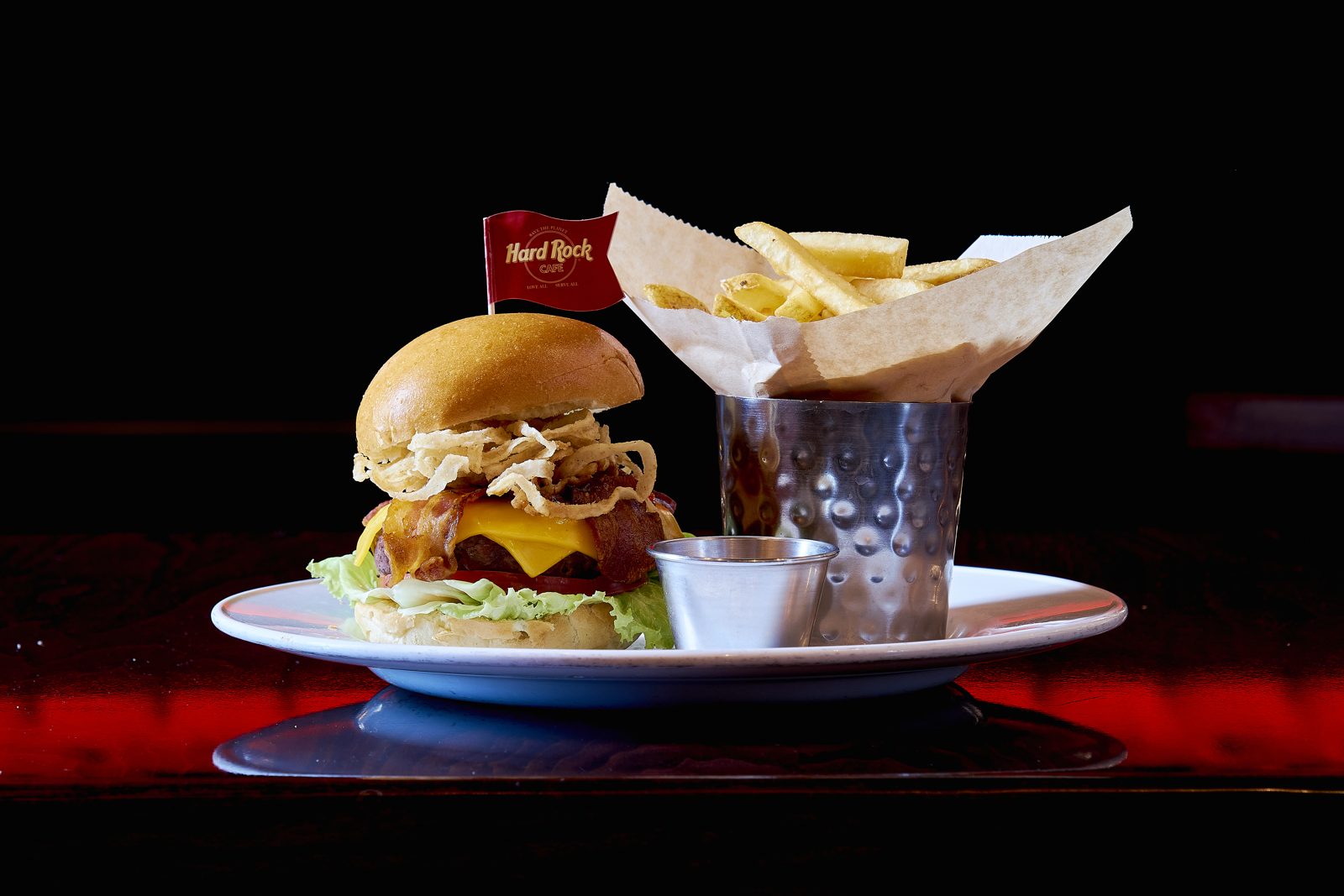 Hamburguesa con bacon, queso y cebolla crujiente junto a patatas fritas, sobre fondo oscuro