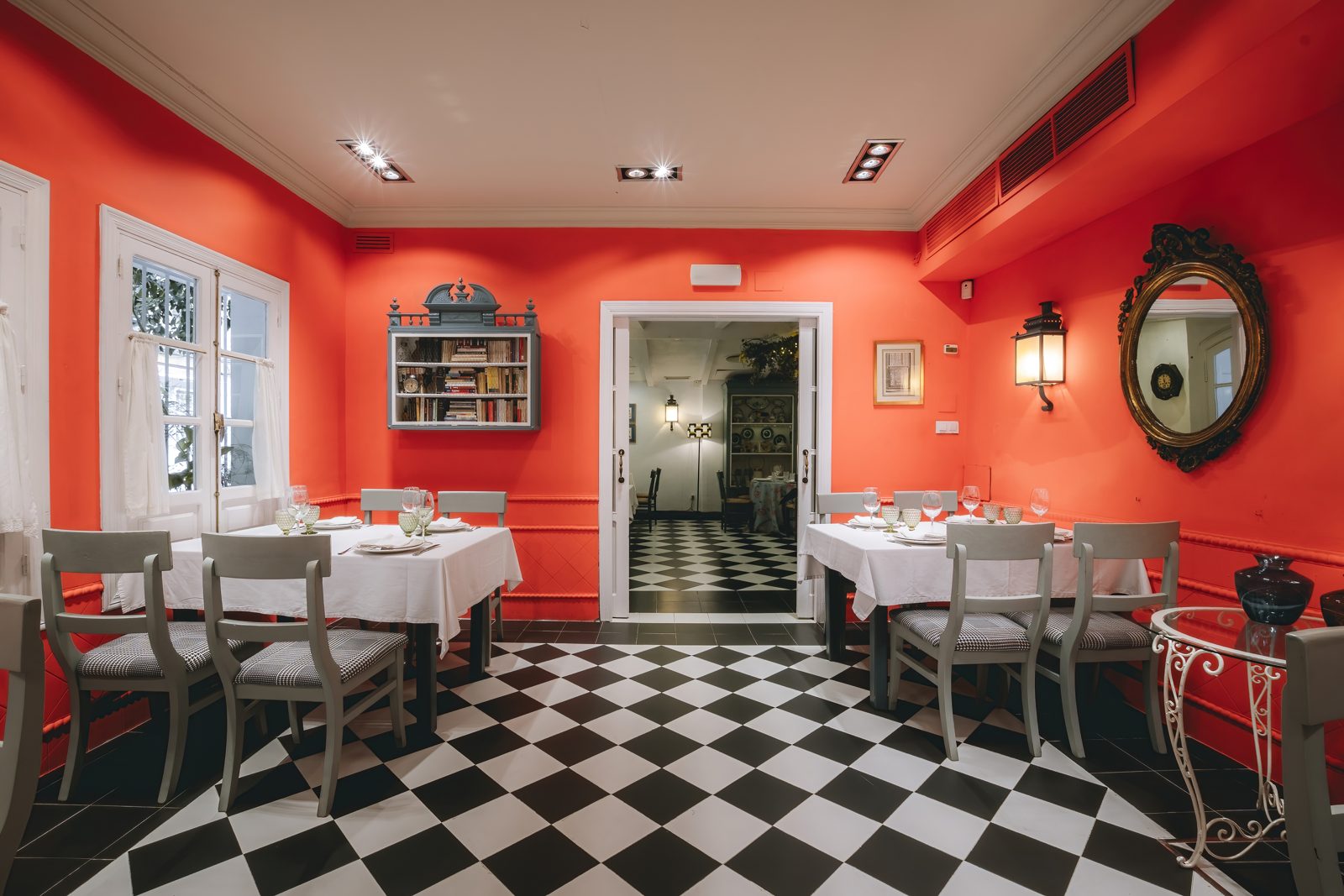 Sala de restaurante con paredes rojas, suelo ajedrezado y mesas con mantel blanco