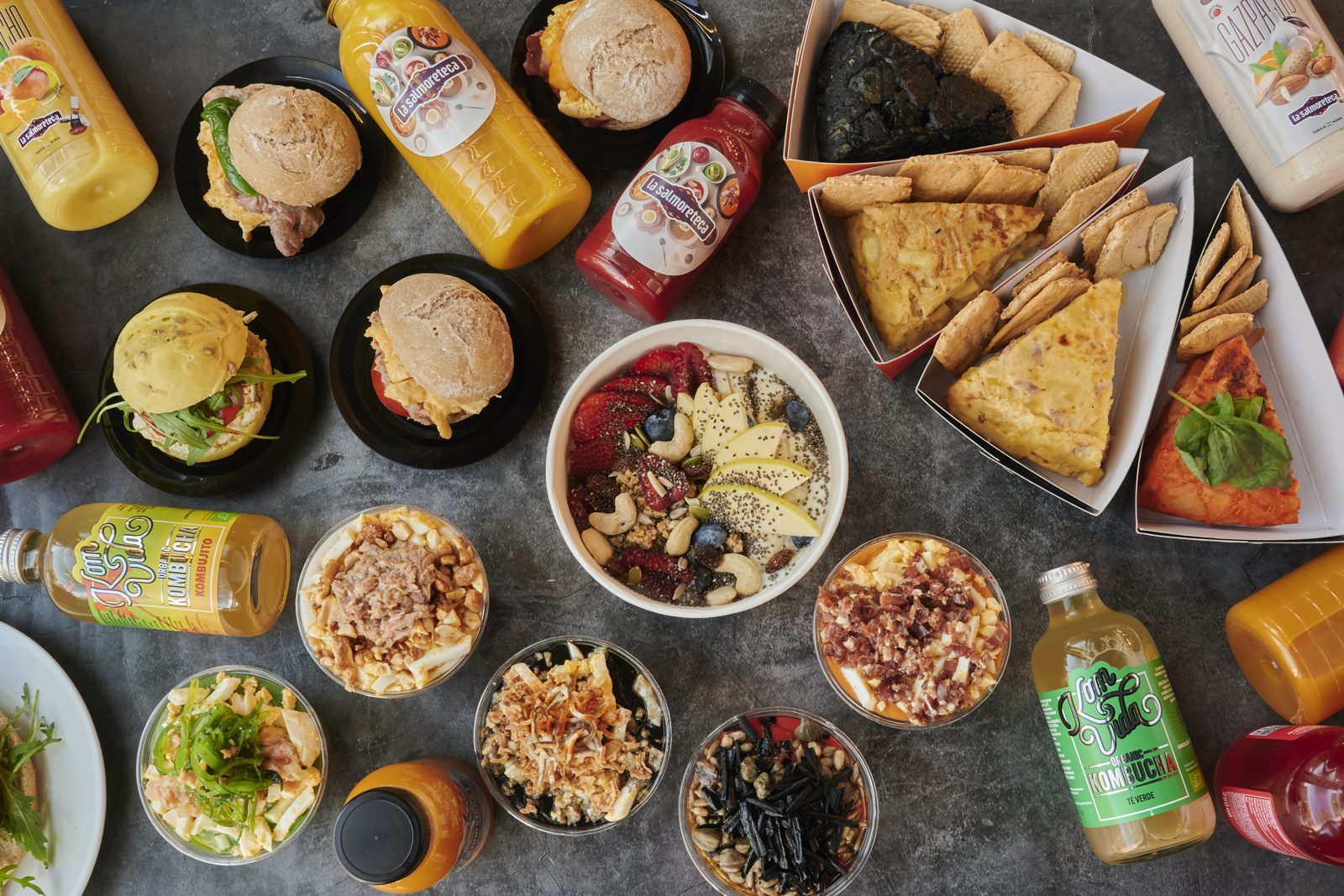 Bodegón cenital de bocadillos, tortillas, bowls y bebidas embotelladas de marca